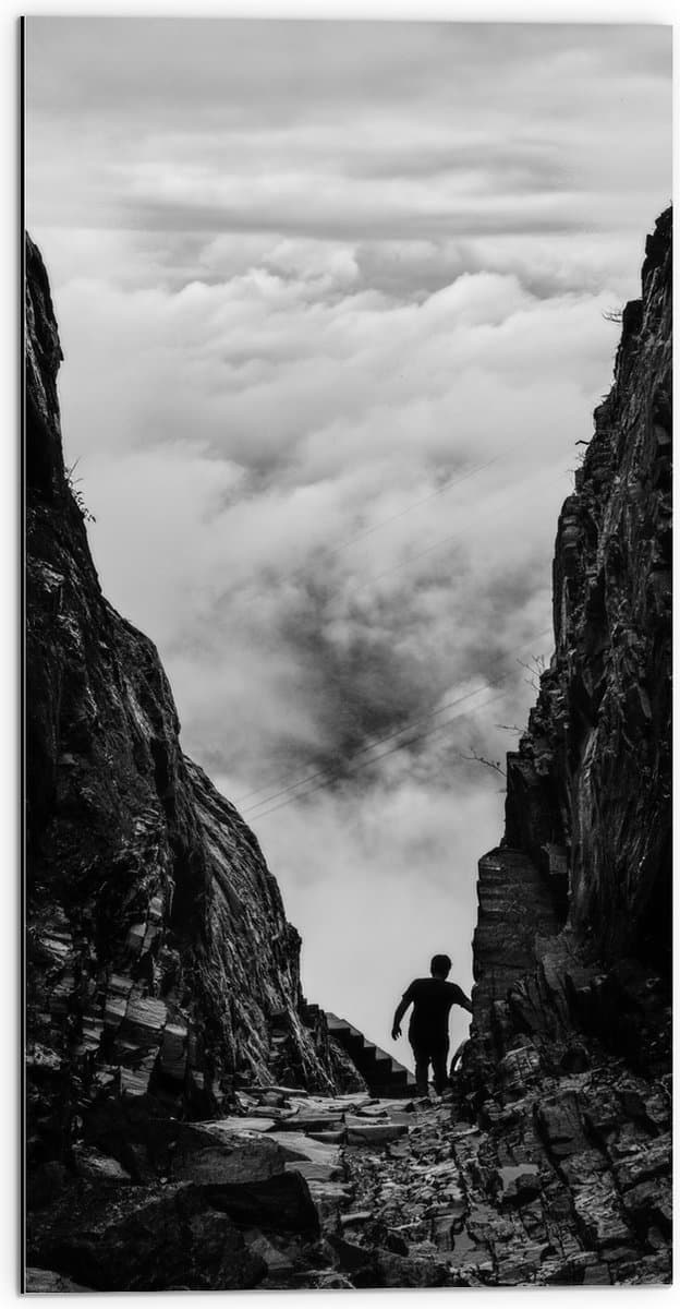Dibond - Man tussen Rotsen boven Wolken in Zwart-wit - 50x100 cm Foto op Aluminium (Wanddecoratie van metaal)